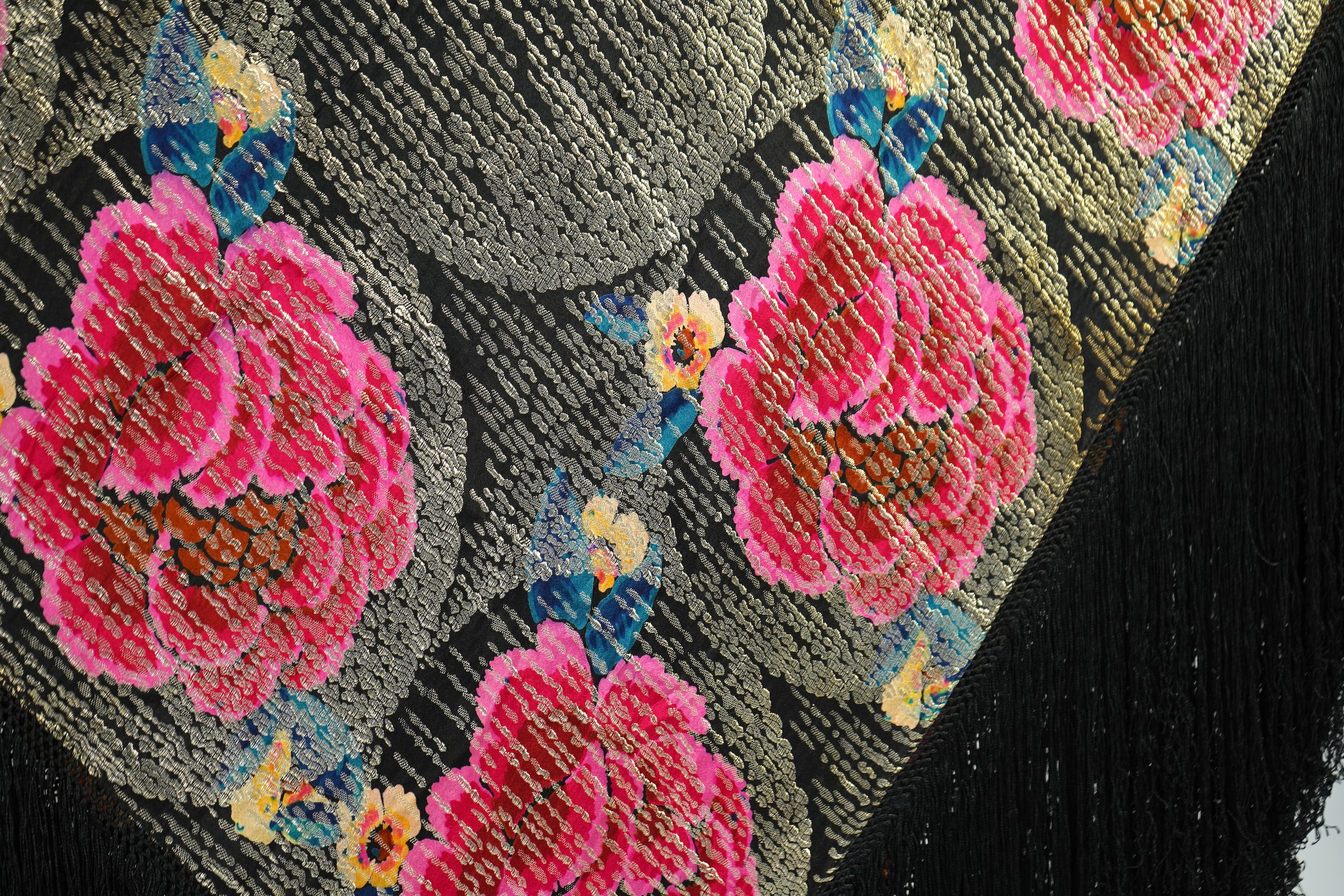 A 1930's ‘jazz age’ black and coloured silk lame evening shawl. Woven with giant pink and red roses and silver thread stripes, edged with long silk fringing. 118cm x 123cm. Condition - colours and silk strong. Fringing g